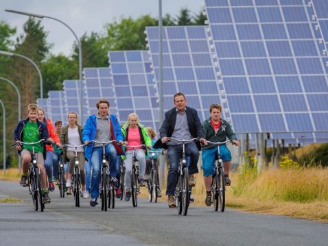 Kinder und Erwachsene fahren Fahrrad vor grossen Solarzellen