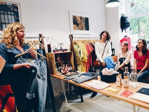Frauen in Kleiderladen hören einer Frau mit Hose in der Hand zu