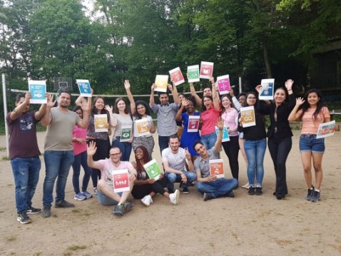 Junge Menschen posieren für das Foto mit SDG Bildern in den Händen auf einem Volleyball Feld